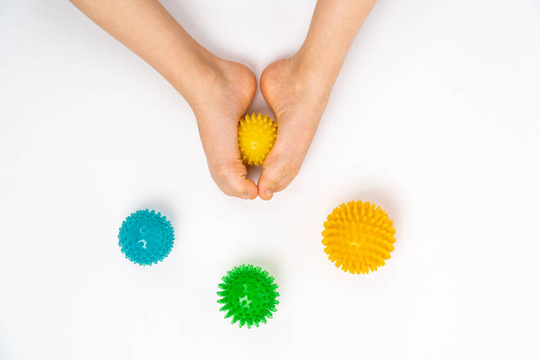 colored needle balls for massage and physiotherapy on a white background with the image of childrens feet, the concept of prevention and treatment of hallux valgus - Foto, Imagem