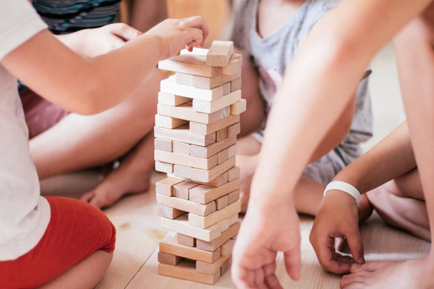 Blurred childrens hands play game with tower, made of wooden blocks - Φωτογραφία, εικόνα