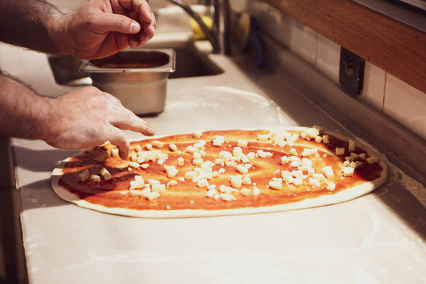 Pizza chef put sauce on base in a commercial kitchen - Fotó, kép