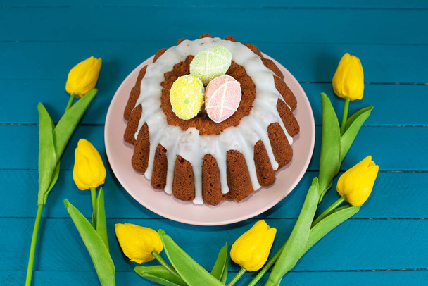 Glazed easter cake decorated with mini eggs araund yellow tulips - Photo, Image