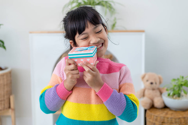 Kis ázsiai lány mosolyog és izgatott és kezében piros ajándék doboz a nappaliban háttérben. gyermek gazdaság ajándék doboz karácsonyra és újévre.ázsiai gyermek lány mosoly és meglepetés. - Fotó, kép