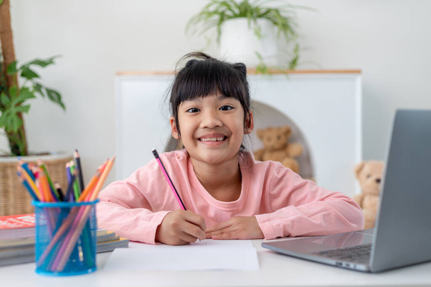 Asian girl using Laptop computer for online study homeschooling during home quarantine. homeschooling, online study, home quarantine, online learning, corona virus or education technology concept - Фото, зображення