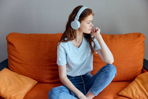 woman sitting on the couch at home listening to music on headphones apartments - Photo, image