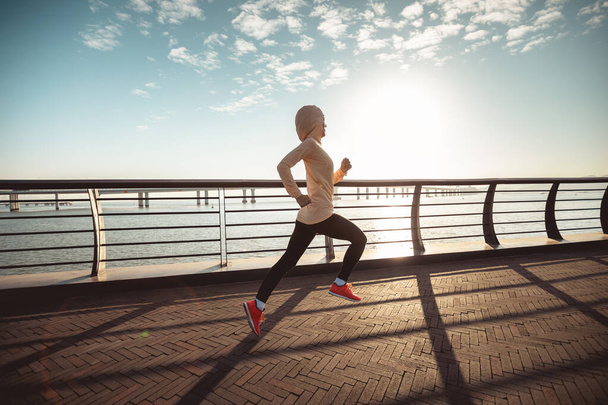 Fitness woman runner running on seaside bridge - Fotó, kép