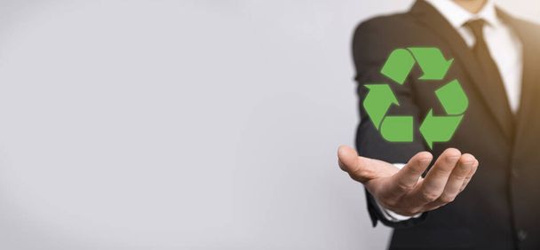 Businessman in suit over grey background holds an recycling icon, sign in his hands. Ecology, environment and conservation concept. - Foto, Imagen