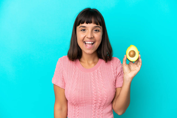 Young mixed race woman holding an avocado isolated on blue background with surprise facial expression - Foto, immagini