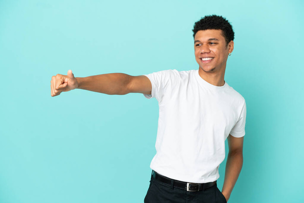Nuori afroamerikkalainen mies sinisellä pohjalla antaa peukalot ylös ele - Valokuva, kuva