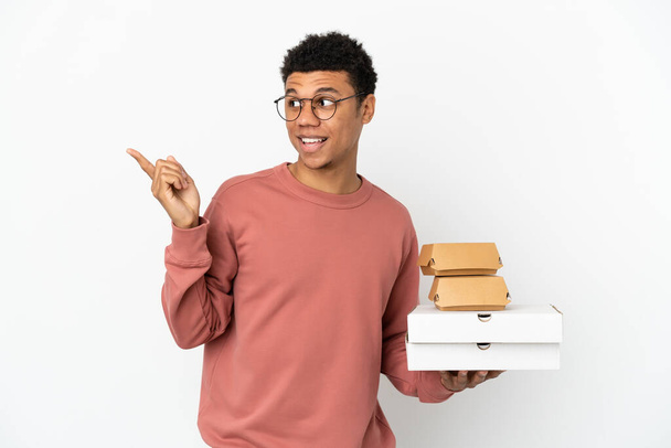 Young African American man holding a burger and pizzas isolated on white background intending to realizes the solution while lifting a finger up - Fotó, kép