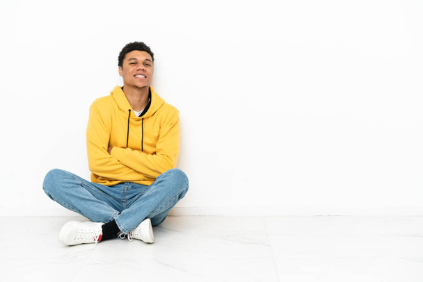 Genç Afrikalı Amerikalı bir adam beyaz arka planda izole bir şekilde oturuyor, kolları bağlı ve ileriye bakıyor. - Fotoğraf, Görsel