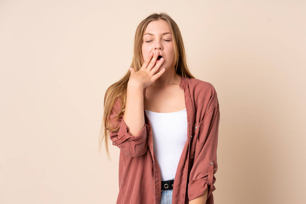 Teenager Ukrainian girl isolated on beige background yawning and covering wide open mouth with hand - Photo, Image