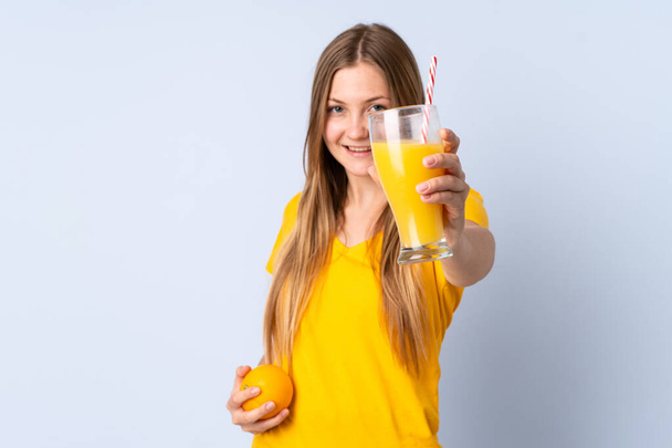Teenager Ukrainian girl isolated on blue background holding an orange and an orange juice - Foto, afbeelding