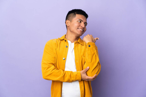 Young Ecuadorian man isolated on purple background pointing to the side to present a product - Foto, afbeelding