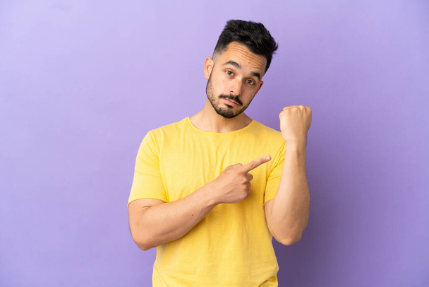 Young caucasian man isolated on purple background making the gesture of being late - Фото, зображення