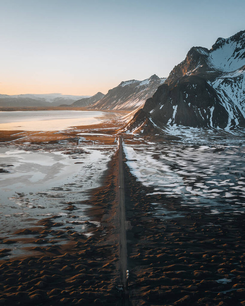 Aerial drone panorama of gravel road at sunset with Vestrahorn mountain and stokksnes beach in Iceland in the background. Winter scenery with snow and sun. - Foto, afbeelding