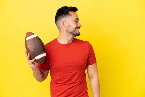 Young Caucasian man playing rugby isolated on yellow background laughing in lateral position - Foto, Bild