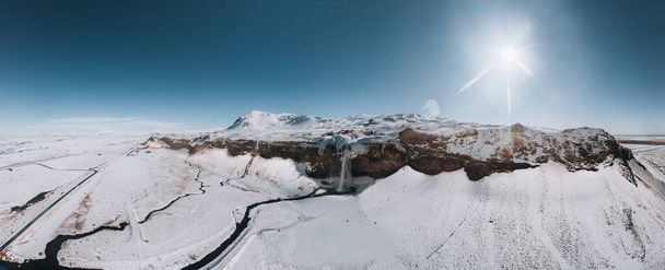 Aerial drone photo of Seljalandsfoss waterfall in Iceland captured in winter. Top view of Nordic majestic waterfall with tourists from above. Winter beauty landscape with frozen water - Foto, immagini