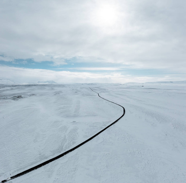aerial drone view Uphill road landscape in winter at Iceland. Asphalt road with sideways full of snow during winter with blue sky. - Φωτογραφία, εικόνα