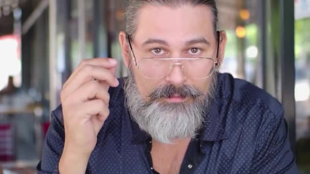 Bearded middle-aged man takes off his glasses, looks at the camera and smiles. Slow motion. - Filmati, video