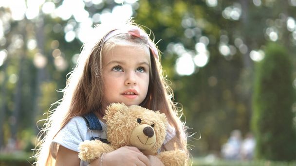 Happy little child girl playing with her favorite teddy bear toy outdoors in summer park - Fotoğraf, Görsel