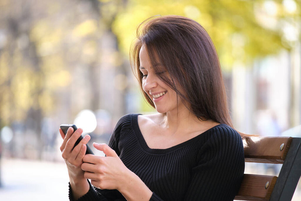 暖かい夏の日に屋外で携帯電話を閲覧路上ベンチに座っている若い女性。通信とモバイル接続の概念 - 写真・画像