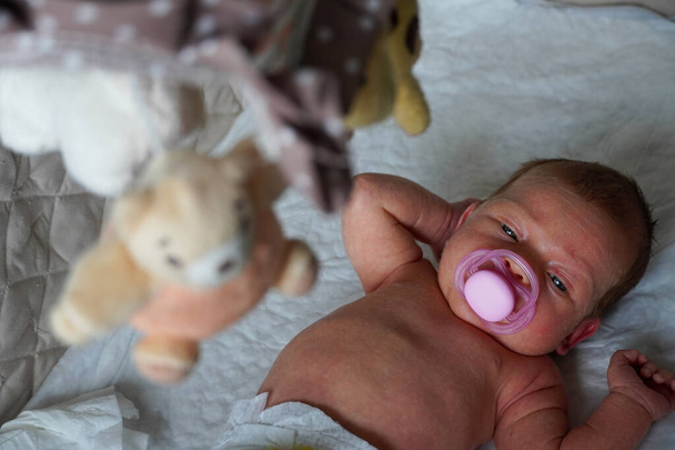 γυμνό μωρό καυκάσιο παιδί με μια πιπίλα στο στόμα του χαλαρώνει ξαπλώνοντας την πλάτη του. - Φωτογραφία, εικόνα