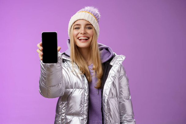 Сасси восторженно веселая женщина рекомендует использовать приложение для редактирования идеальных фотографий, держа в руках смартфон, показывающий дисплей мобильного телефона с гордо удовлетворенной улыбкой камеры, стоящей на фиолетовом фоне - Фото, изображение