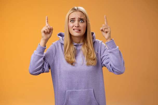 Worried perplexed unsure cute blond woman presenting project standing awkward afraid humiliation crining scared pointing up raised index finger waiting reply nervously, orange background - Fotoğraf, Görsel
