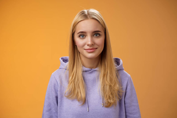 Pas-up delikátní něžné přátelsky vypadající blond evropské dívky v mikině usmívající se podporující mluvení naslouchání přátelé příběh pěkný zajímavý rozhovor stojící ležérně oranžové pozadí - Fotografie, Obrázek