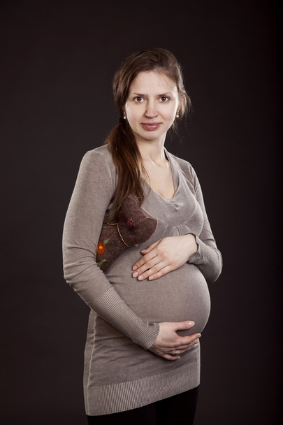 Beautiful pregnant woman in a gray dress with a toy cat - Valokuva, kuva