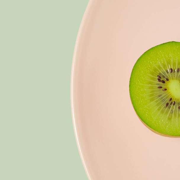 Fruto kiwi medio macro en un plato de color rosa pastel. Fruta dieta concepto mínimo. - Foto, imagen