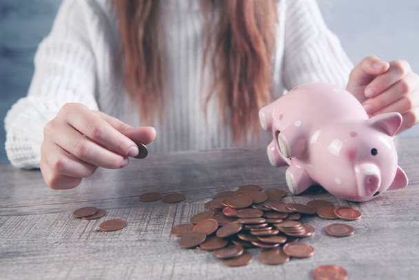 γυναίκα που μετράει νομίσματα στο τραπέζι και δίπλα σε έναν κουμπαρά - Φωτογραφία, εικόνα