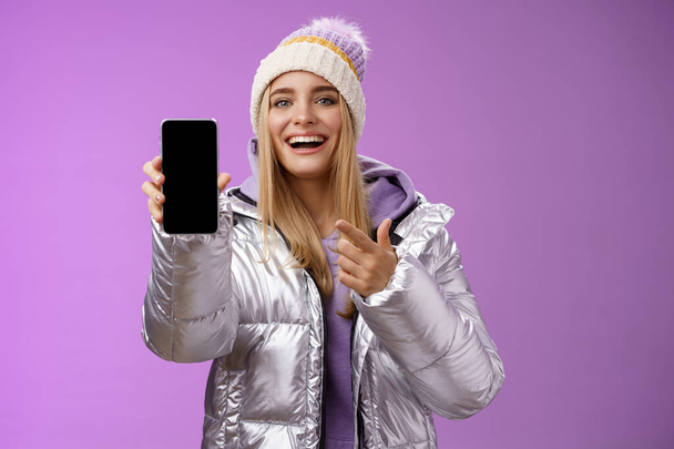 Tevreden geamuseerd goed uitziende blonde meisje suggereren neem kijkje smartphone display glimlachen gelukkig wijzen mobiele telefoon blij praten over geweldige nieuwe app functies, staande paarse achtergrond - Foto, afbeelding