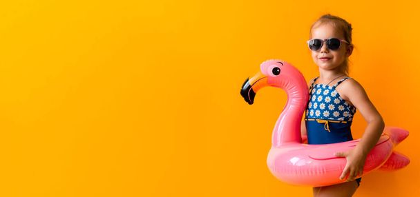 баннер счастливый маленький ребенок пловец спорт девочка носить солнцезащитные очки купальник, ребенок надувной плавательное кольцо розовый фламинго, изолированный оранжевый фон, горячий летний отдых хобби концепции. Копировальное пространство - Фото, изображение
