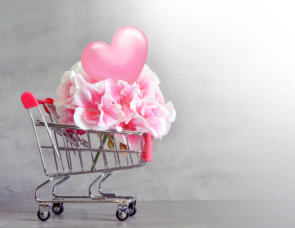 Shopping trolley with flower and hearts isolated on grey background. Shopping concept. - Valokuva, kuva
