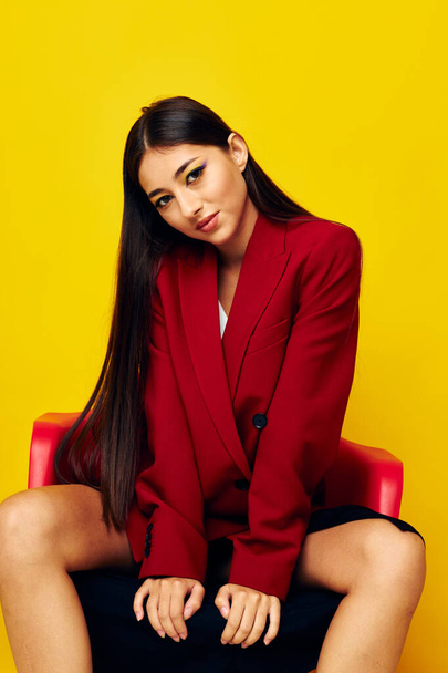 pretty brunette in a red jacket sits on a chair yellow background - Foto, immagini