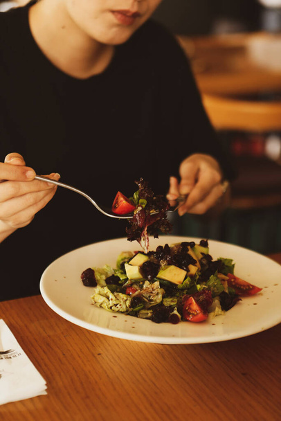 Portrait of attractive caucasian smiling woman eating salad, focus on hand and fork. - Photo, image