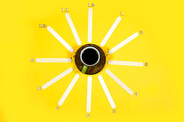 foto creativa di tazza di caffè nero con bastone di legno formando un orologio su sfondo giallo - Foto, immagini