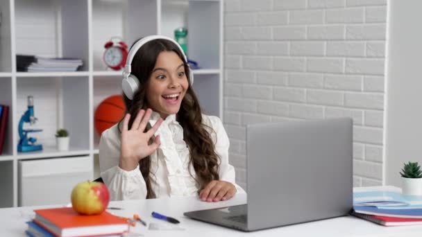 niño feliz en los auriculares estudio en la escuela lección en línea con el ordenador diciendo hola, videollamada - Imágenes, Vídeo