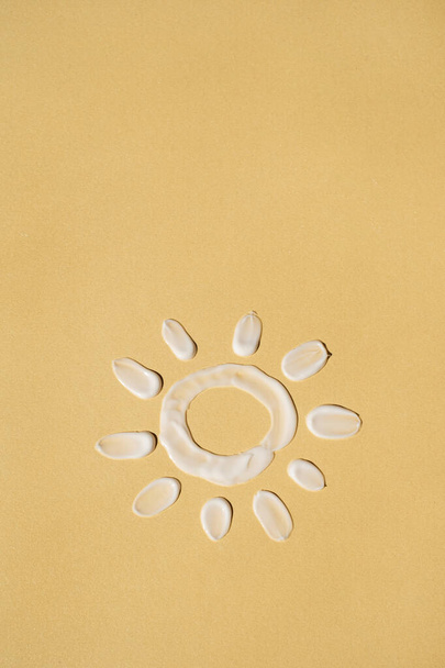 Beauty, skincare product setting. Sun symbol made of white cosmetic cream smear on pastel yellow background - Photo, Image
