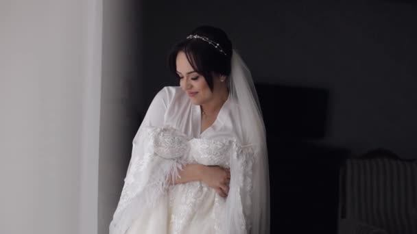 Невеста в нижнем белье стоит со своим свадебным платьем у окна дома, белое будуарное платье и вуаль - Кадры, видео