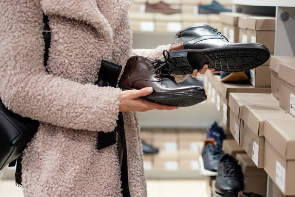 young woman in faux fur coat chooses for man shoes in shoe department in shopping mall, unrecognizable person. Shopping time - 写真・画像
