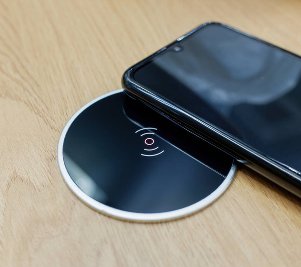 wireless charging for a smartphone built into a wooden office desk next to a black smartphone - Fotó, kép