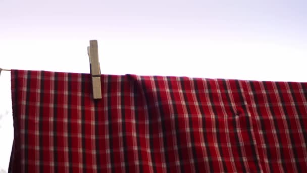Shirts and pants are hanging on the clothesline after being washed hold by wooden pins in closeup - Metraje, vídeo