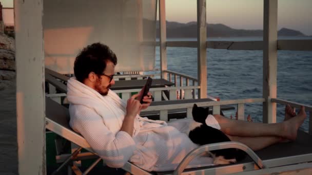 De mens rust op de zonnebank op een pier naast de zee en wordt woedend na mobiel bellen. - Video