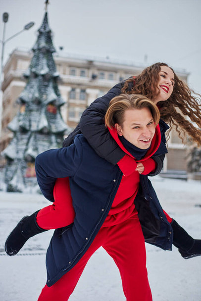 Genç bir aile babası ve kız, karlı bir günde günü parkta geçirirler. Kış şehrinde yürürken eğlenen duygusal genç çift, neşeli bir adam, gülen güzel kadınına sarılır.. - Fotoğraf, Görsel