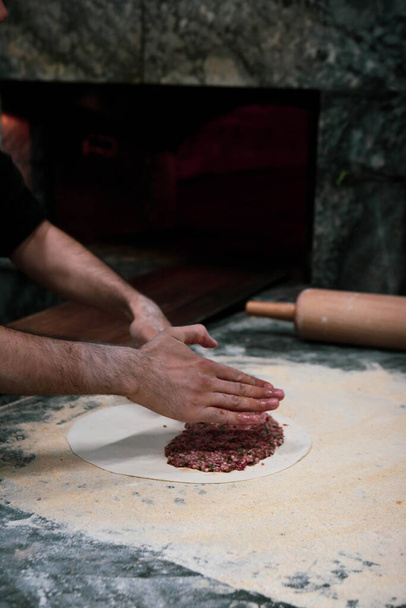 Török pizza vagy lahmacun készítése - gyorsétterem és népszerű utcai ételek a mediterrán országokban. Tészta, darált hús és növényi összetevők a török pide főzéséhez. - Fotó, kép