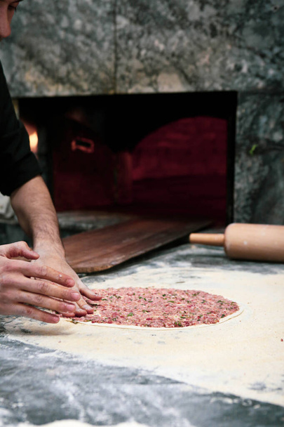 Robienie tureckiej pizzy lub lahmacun - fast food i popularne uliczne jedzenie w krajach śródziemnomorskich. Ciasto, mięso mielone i składniki roślinne do gotowania tureckiej pidy. - Zdjęcie, obraz