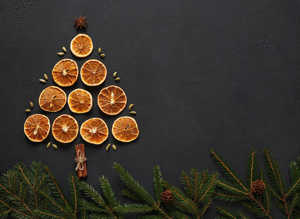 αποξηραμένες φέτες πορτοκαλιού λάι με τη μορφή χριστουγεννιάτικου δέντρου σε σκούρο πίνακα με γλυκάνισο αστέρια, ξυλάκια κανέλας, κλαδιά ελάτης, πάνω όψη. αντίγραφο χώρου - Φωτογραφία, εικόνα