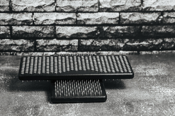 Close-up black Sadhu wooden boards with nails for yoga and spiritual practices on the grey background and dark brick wall. The concept of meditation, standing on nails, therapy. - Photo, Image