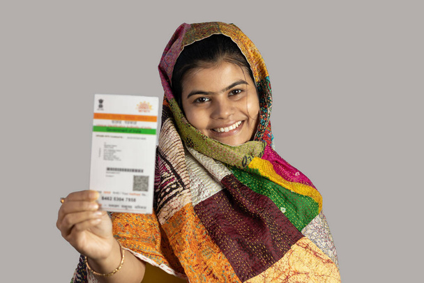Una giovane donna indiana sorridente con carta Aadhaar in mano su sfondo bianco - Foto, immagini